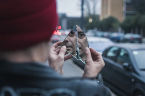 Парень-панк смотрит на себя в разбитое зеркало — стоковое фото