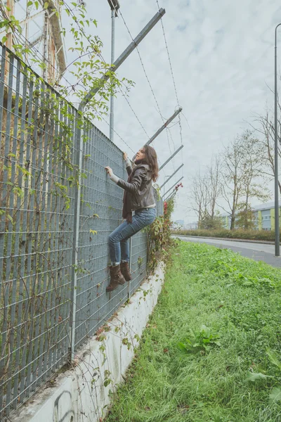 Linda jovem morena escalando por cima de uma cerca — Fotografia de Stock