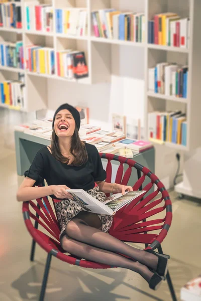 Beautiful young brunette sitting in a bookstore — Stock Photo, Image