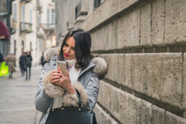 Beautiful young brunette texting in the city streets — Stock Photo, Image