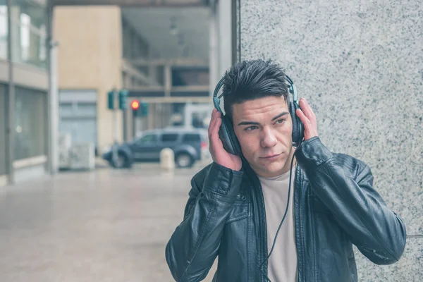 Mladý pohledný muž se sluchátky pózuje v ulicích města — Stock fotografie