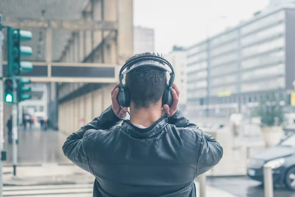 Vista posteriore di un giovane uomo con le cuffie in posa in città stre — Foto Stock