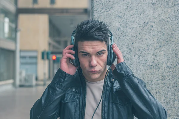 Mladý pohledný muž se sluchátky pózuje v ulicích města — Stock fotografie