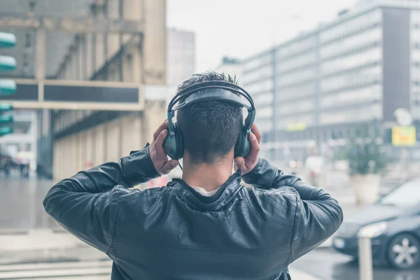 Vista posteriore di un giovane uomo con le cuffie in posa in città stre — Foto Stock