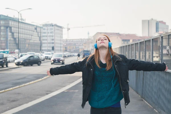 Vacker flicka med hörlurar poserar i stadens gator — Stockfoto