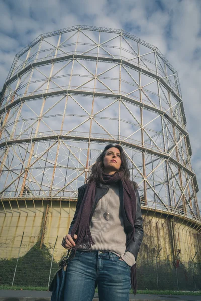 Beautiful young brunette posing in front of a gasometer — Stock Photo, Image