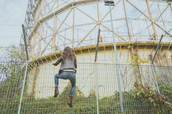 Beautiful young brunette climbing over a fence — Stock Photo, Image