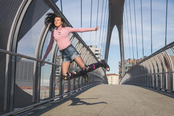 Beautiful young brunette jumping on a bridge — Stock Photo, Image