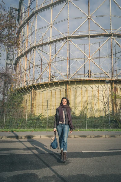 Beautiful young brunette posing in front of a gasometer — Stock Photo, Image