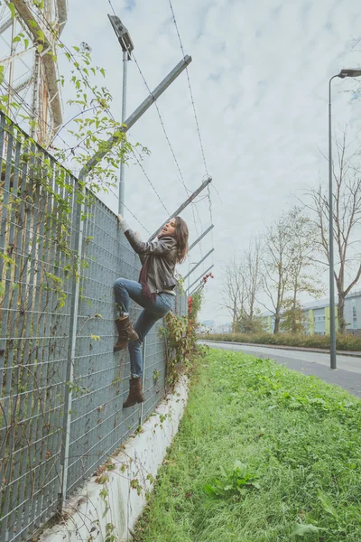 Beautiful young brunette climbing over a fence — Stock Photo, Image