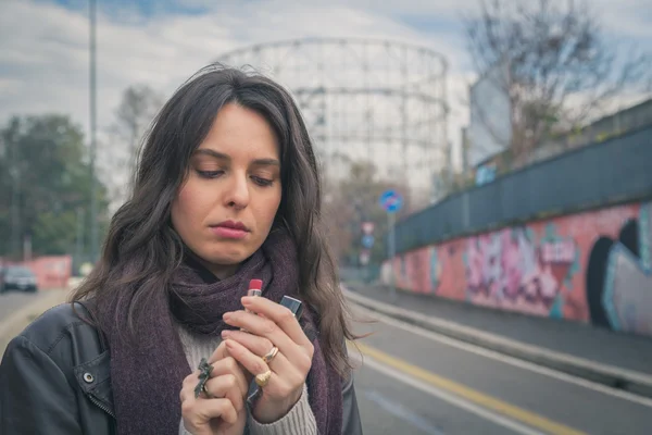 Bella giovane bruna che si mette il rossetto nelle strade della città — Foto Stock