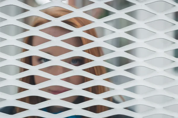 Redhead girl posing behind a grate — Stock Photo, Image