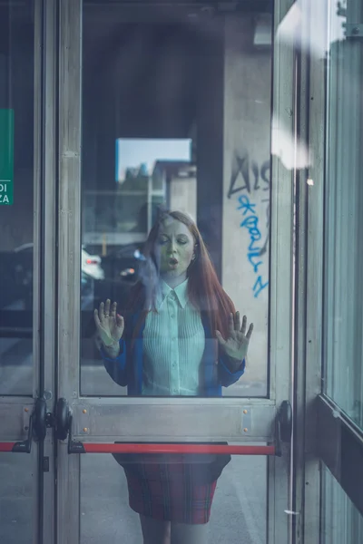 Menina ruiva bonita posando atrás de uma porta de vidro — Fotografia de Stock