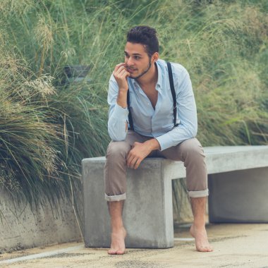 Beton bir bankta oturan genç yakışıklı adam