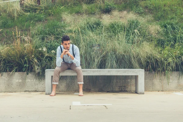 Junger schöner Mann sitzt auf einer Betonbank — Stockfoto