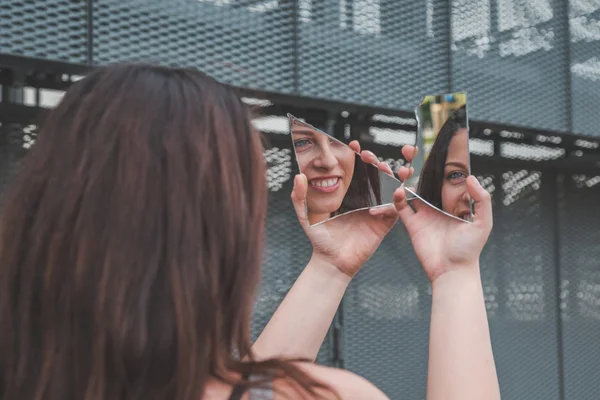 Beautiful girl looking at herself in a broken mirror — Stock Photo, Image