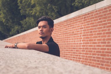 Yakışıklı Asya model arka planda bir tuğla duvar ile poz