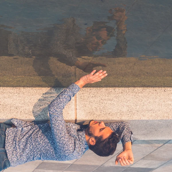 Junger schöner Mann, der sich im Wasser selbst betrachtet — Stockfoto