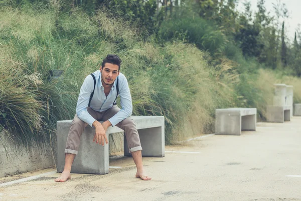 Junger schöner Mann sitzt auf einer Betonbank — Stockfoto