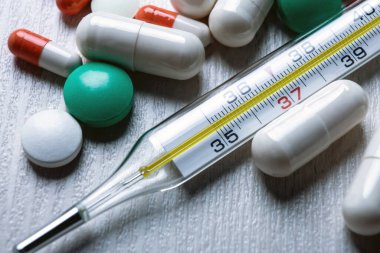 Civa tıbbi termometre ve masadaki haplar yakın plan.