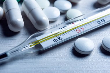 Civa tıbbi termometre ve masadaki haplar yakın plan.