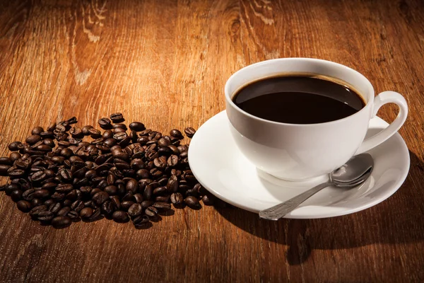 Bodegón con una taza de café negro y granos de café tostados — Foto de Stock