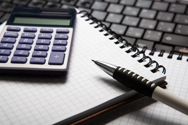 Pluma con calculadora en un cuaderno y teclado — Foto de Stock