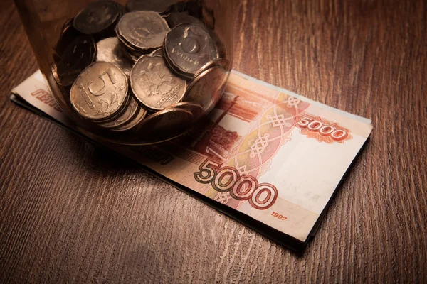 Bundle of bank notes and a glass jar with coins — Stock Photo, Image