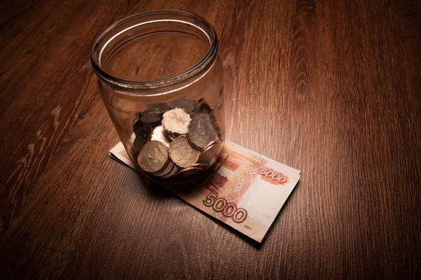 Bundle of bank notes and a glass jar with coins — Stock Photo, Image