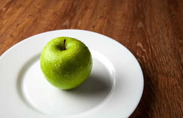 Färskt grönt äpple på en vit platta — Stockfoto