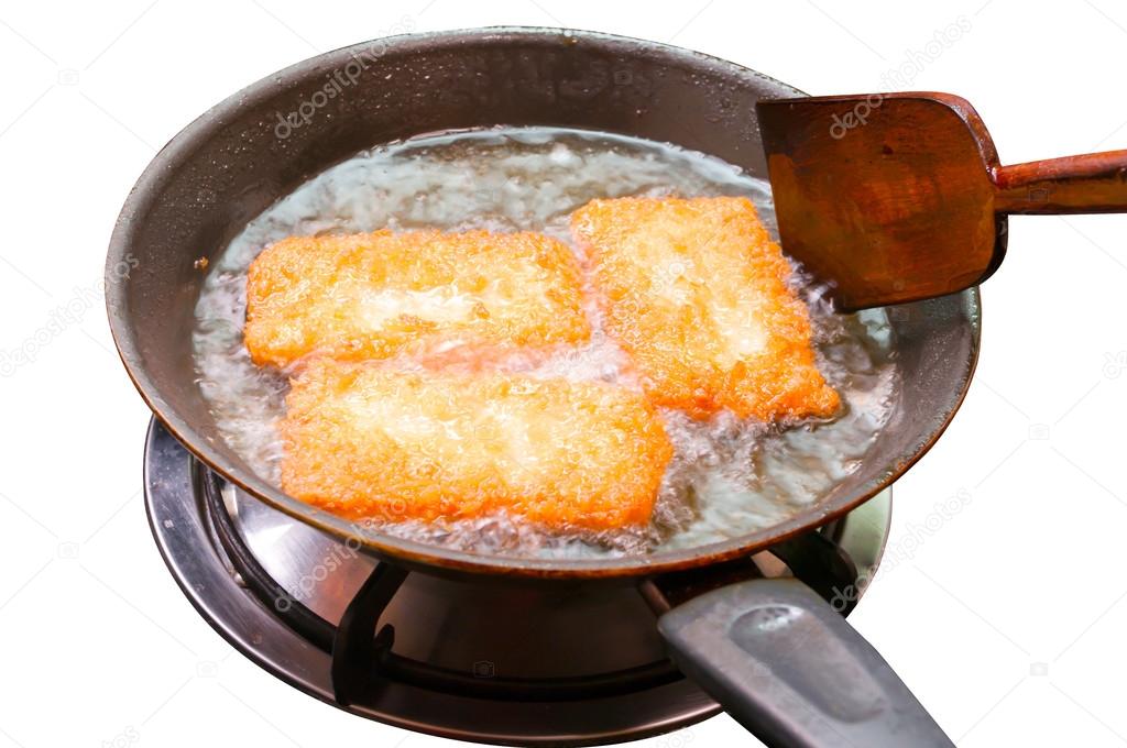 breaded chicken pieces being deep fried in a cast iron pan