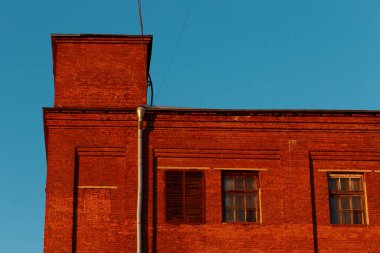 Açık mavi gökyüzüne karşı kırmızı tuğlalı endüstriyel bir binanın yakın plan görüntüsü..