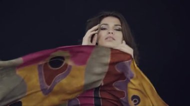 Muhteşem saçlı bir kız, parlak, büyük, renkli bir atkıyla dans ediyor. Tekstil ve kumaş reklamları. Ağır çekim. Duygu.