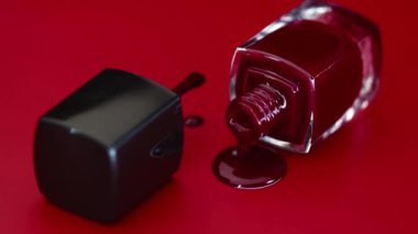 Kırmızı arka planda bir şişe tırnak cilası var. Kırmızı yüzeye kırmızı oje damlıyor. Kavram. Manikür ustası..