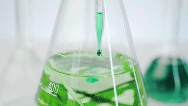 実験室のフラスコには 澄んだ液体と生きた藻類があります 医療用手袋の手はガラスフラスコに液体を滴下しています 海洋植物由来の天然化粧品の生産 — ストック動画
