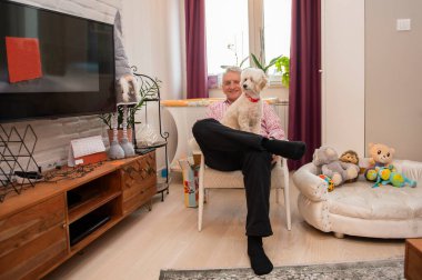 Oturma odasında kaniş köpeği olan beyaz yaşlı bir adamın portresi. Mutlu bir yaşlılık konsepti.