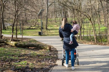 Bir anne parkta yürürken kızını kollarına alır.