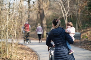 Bir anne parkta yürürken kızını kollarına alır.