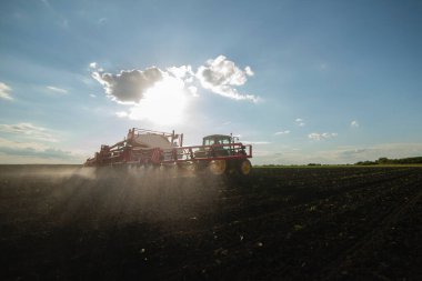 İlkbaharda tarlada toprak püskürten traktör.