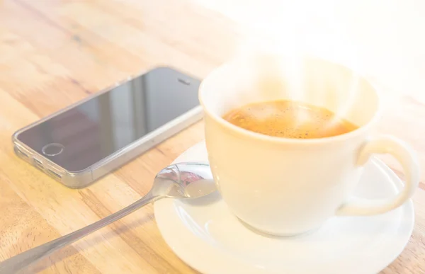 Telefone celular e xícara de café na mesa de madeira do escritório — Fotografia de Stock