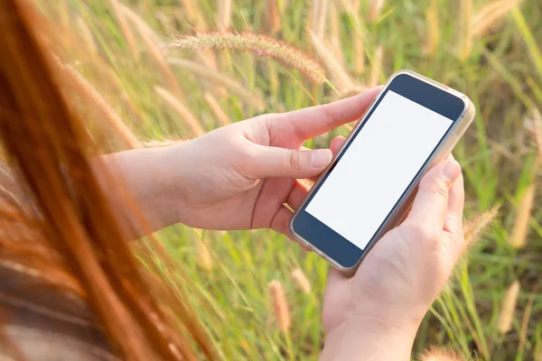使用智能手机上草鲜花背景的女人 — 图库照片
