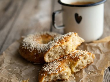 Tahta zemin üzerinde susamlı taze peynirli çörekler ve metal beyaz kahve fincanı. Sağlıklı yemek, diyet, kahvaltı, öğle yemeği. Kopyalama alanı olan üst görünüm. retro, vitage.