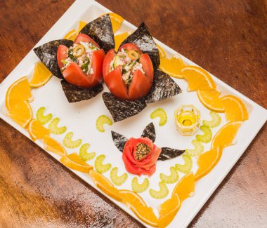 Yıldız kesimi kırmızı domatesler ve deniz yosunları üzerinde sunulan balık ceviche yanında zencefil, turuncu ve yeşil zeytin, beyaz bir tabak ve ahşap bir arka planda sunuluyor.