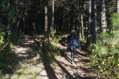 Maceracı bir kızın portresi, yeni yollar keşfediyor, siyah giyinmiş, mavi bir sırt çantası, şapka ve siyah bir sırt çantasıyla..