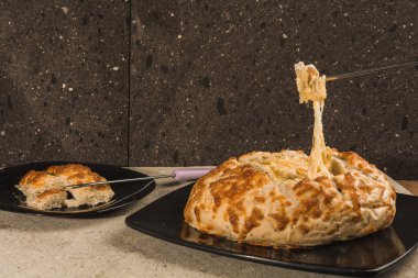 Tahıl ekmeği, fondü peynirini siyah tabaklara ve taş ocağının arka planına koymak için ortadan kesilmiş. Bir kadın eli, erimiş peynirle birlikte ekmeğin parçalarını çatalla ayırır. 2