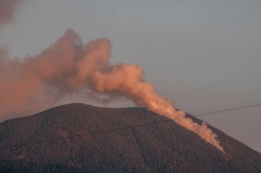 Dağın tepesindeki orman yangını, ağaçlar ve orman yanıyor, gün batımı ışığı ılık renkleriyle oynuyor.. 