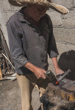 Demircide çalışan demirci, metali aletin içine sokarak keski yapmak için parlak bir metalle çalışıyor.. 