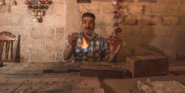 Atölyesinde yılbaşı topları yaratmak için cam üfleyen bir zanaatkar, bir kaynak makinesinin yardımıyla cam tüpleri farklı şekillerde şekillendiriyor..