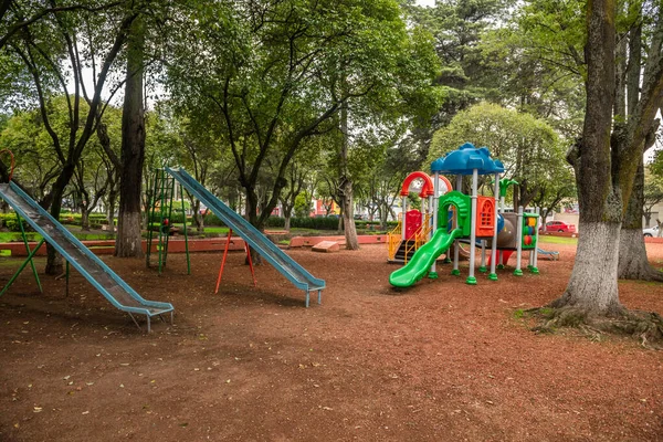 Playground in an open-air park, there are slides, swings, castles, the many colors that the games have contrast with the natural tones of the park.