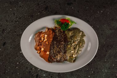 Enmoladas de encacahuatado, mole negro, pipian served on the same white plate, stuffed with chicken.